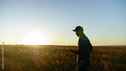 Farmer businessman is working on tablet computer while standing in middle wheat field at sunrise. Man uses tablet tapping screen, plans to harvest. Concept technology in agriculture, farming