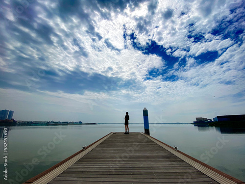 Against the background of blue sky and white clouds, an Asian woman stood on a trestle by the lake and looked up at the sky