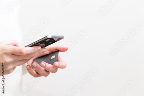 Close up of female hands holding credit card and using smartphone on white background. Woman paying securely online, using banking service, ordering in internet store. Online shopping