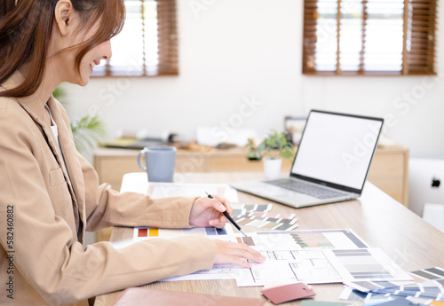 Professional interior designer working in the office  Portrait of young asian female architect working on business of Real estateproject   sketching on a house plan choosing swatches and material..