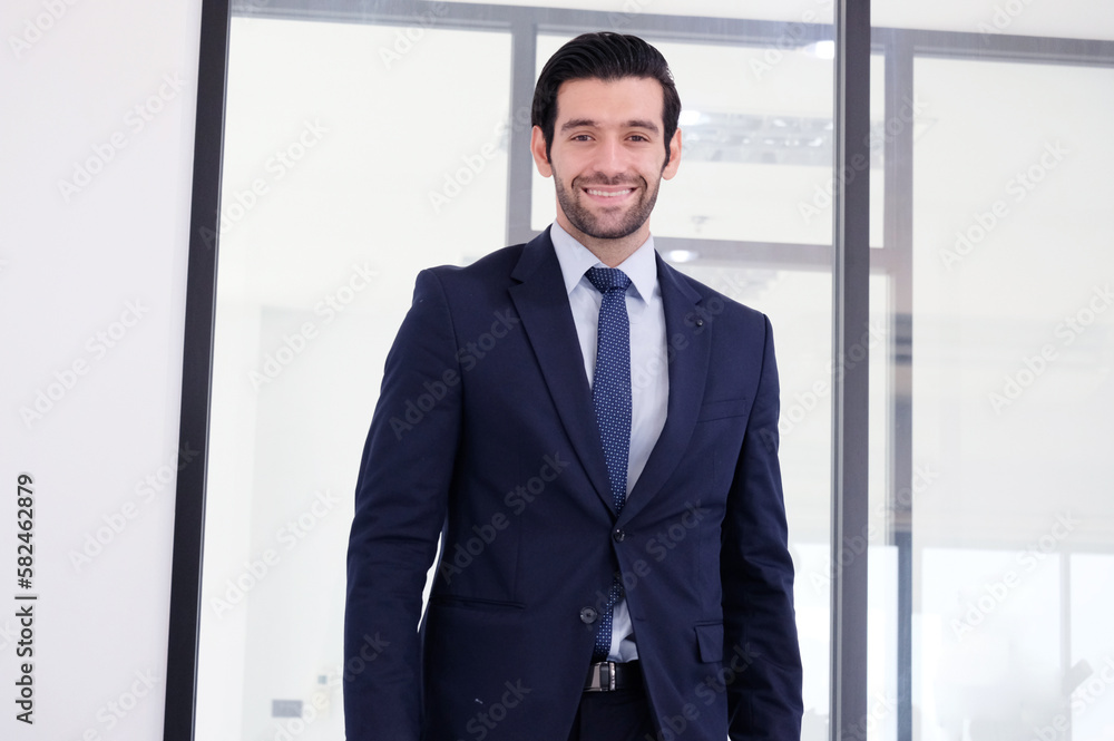 Handsome young businessman in suit standing smiling inside office. Handsome young businessman in suit standing smiling inside office.