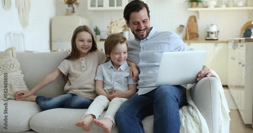 Happy daddy and two cute little sibling kids using online app on laptop for communication, watching cartoon funny movie, sitting with laptop on comfortable sofa Happy daddy and two cute little sibling kids using online app on laptop for communication, watching cartoon funny movie, sitting with laptop on comfortable sofa
