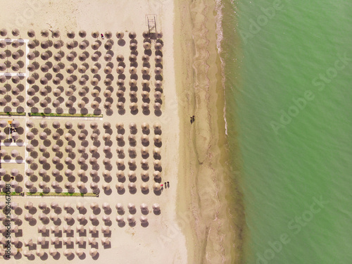 View from above on a beautiful beach with clear blue water. Raws of beach umbrellas on the shore. Summer season concept