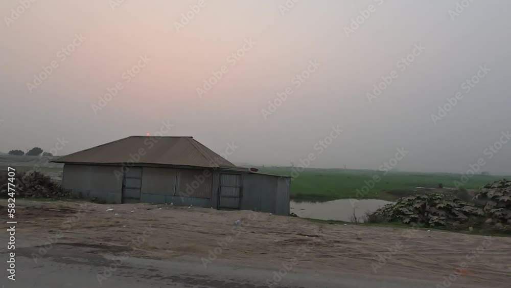 Beautiful sunset view in a rural area 4K video. Countryside road trip footage at dusk time. Beautiful meadow, brick kiln, and sunset view from a moving vehicle. Village road trip 4K footage.