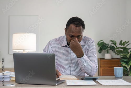 Stressed business man sitting at office workplace. Tired and overworked black man. Young african-american exhausted men in stress working on laptop computer