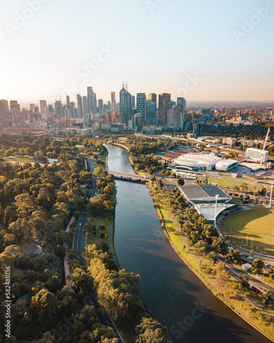 Drone vertical shot of the Melbourne cityscape with a river and green trees on a sunny day