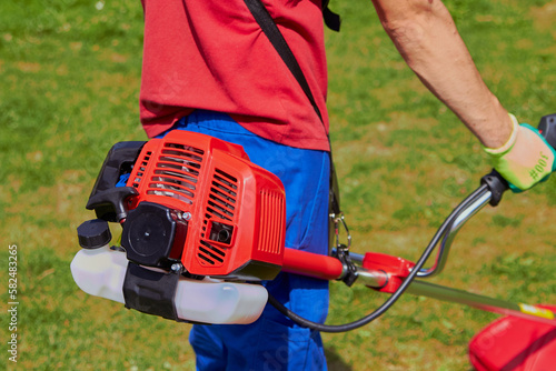 gardener with a brush cutter in the garden,a man holds a gasoline trimmer in his hands, a close-up of a motor mower from the side of a man mowing grass