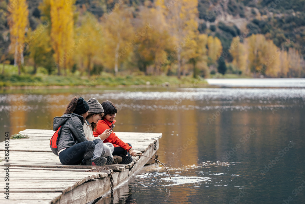 Shot of pretty family looking at the horizon sitting on a pier on the lake Shot of pretty family looking at the horizon sitting on a pier on the lake