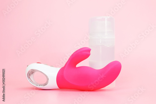 Waterproof adult sex toy from body-safe silicone and lubricant on pink background. G-spot vibrator with clitoral stimulator from medical grade silicone. Bendy vibrator with clitoral stimulation arm