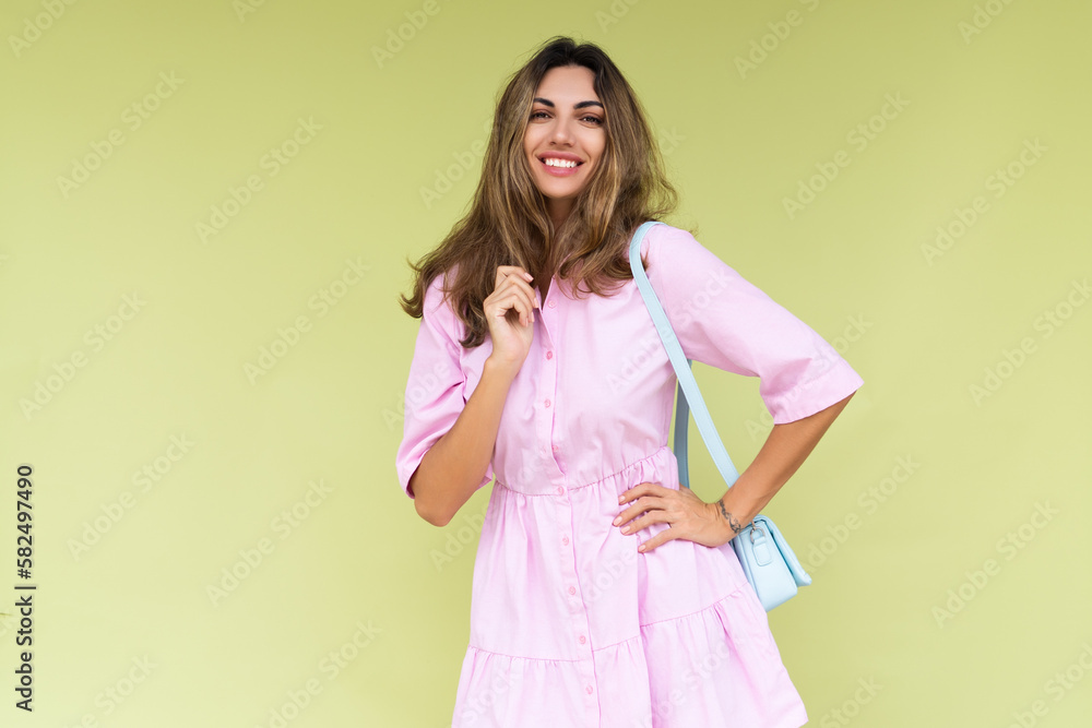 Young woman in casual pink summer cotton dress wear isolated on green background holding cute blue shoulder bag happy big smile Young woman in casual pink summer cotton dress wear isolated on green background holding cute blue shoulder bag happy big smile