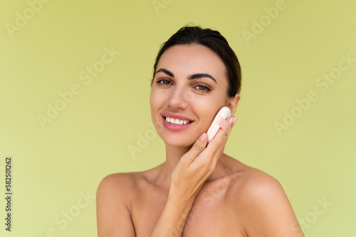 Beauty portrait of young woman with bare shoulders on green background with cosmetic powder puff velour makeup foundation blender sponge applicator