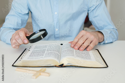 Christian catholic man with magnifying glass searching for answers in old Holy Bible. Loupe on a Bible.