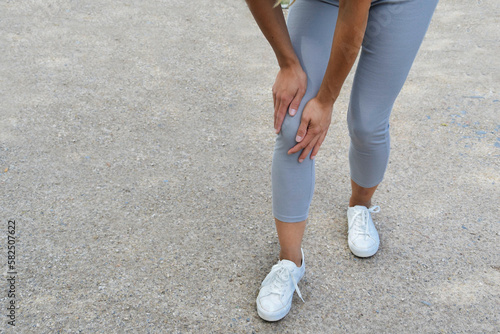 Uraz kolana. Młoda kobieta podczas treningu fitness w parku cierpi z powodu bólu kolana. Knee injury. A young woman suffers from knee pain during fitness training in the park.