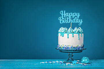 White happy birthday cake with teal ganache over a blue background
