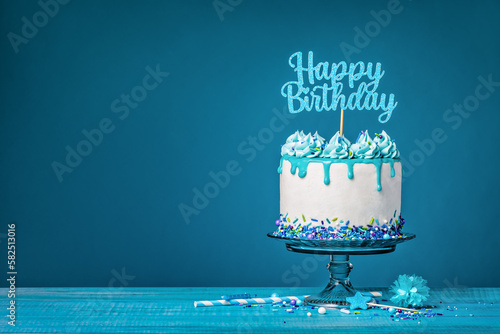 White happy birthday cake with teal ganache over a blue background