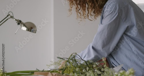 female doing new bouquet. Girl working in flower shop studio. Female florist artist cleans flowers for a beautiful bouquet, workplace view. High quality 4k footage