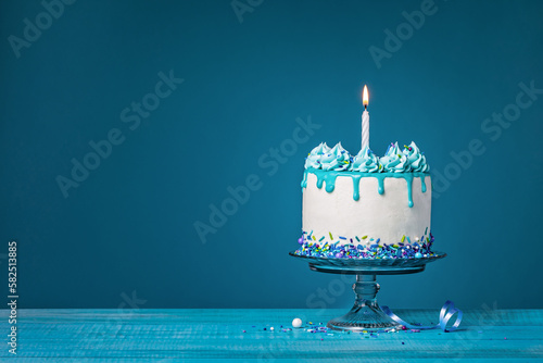White cake with one lit birthday candle on a blue background