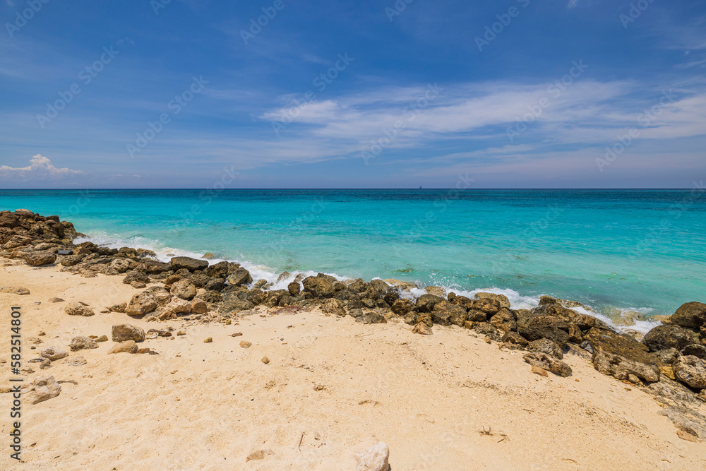 Beautiful view of big rocks protecting sandy coastline. Turquoise water of Atlantic ocean. Aruba. 