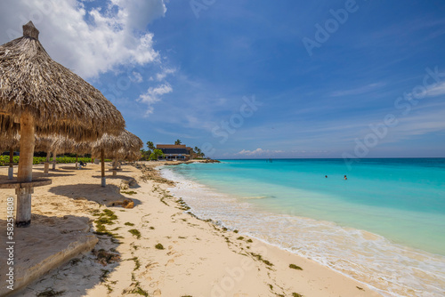 Fototapeta Naklejka Na Ścianę i Meble -  Gorgeous view of Atlantic ocean and Eagle Beach with sun loungers and umbrellas against backdrop blue sky with white clouds. Aruba.