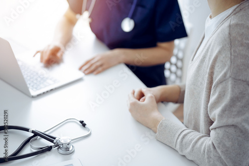 Stethoscope lying on the tablet computer in front of a doctor and patient using laptop computer at the background. Medicine, healthcare concept