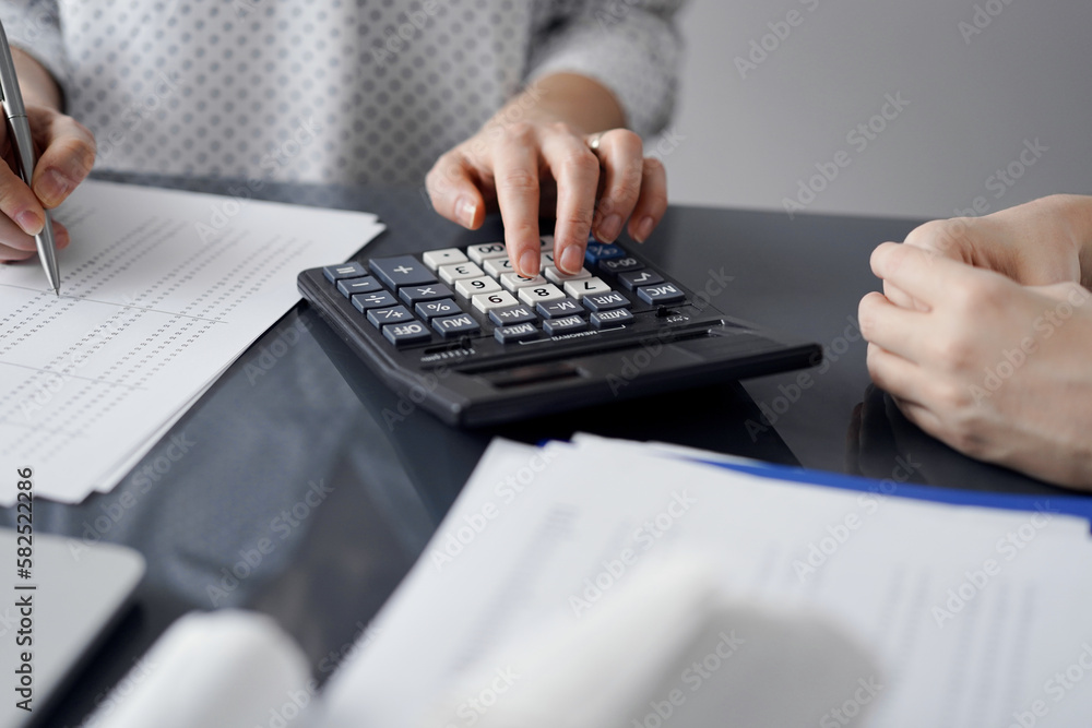 Woman accountant using a calculator and laptop computer while counting taxes for a client. Business audit and finance concepts Woman accountant using a calculator and laptop computer while counting taxes for a client. Business audit and finance concepts