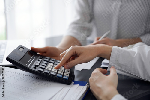 Woman accountant using a calculator and laptop computer while counting taxes for a client. Business audit and finance concepts