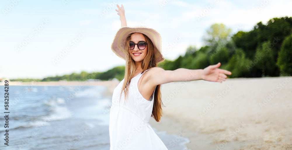 Happy smiling woman in free happiness bliss on ocean beach standing with a hat, sunglasses, and rasing hands. Portrait of a multicultural female model in white summer dress enjoying nature. Happy smiling woman in free happiness bliss on ocean beach standing with a hat, sunglasses, and rasing hands. Portrait of a multicultural female model in white summer dress enjoying nature.