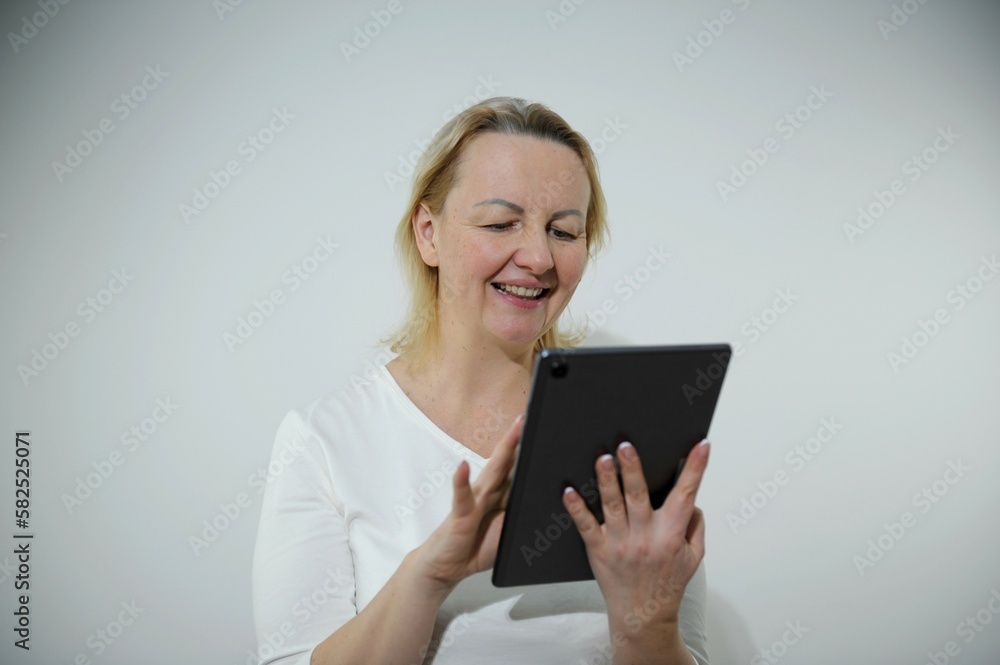 adult satisfied Woman smiles and looks at tablet she leafs through something with hand happy and sincere smile calm look adult satisfied Woman smiles and looks at tablet she leafs through something with hand happy and sincere smile calm look