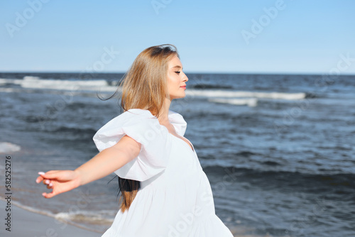 Happy, beautiful woman on the ocean beach standing in a white summer dress, open arms © rogerphoto