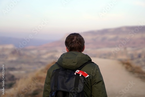 Young Male Tourist Hiking with Backpacks on Top of Rocky Canyon Valley in Front of a city Goreme Cappadocia view in the Mountains of National Park. © MishaelPervak
