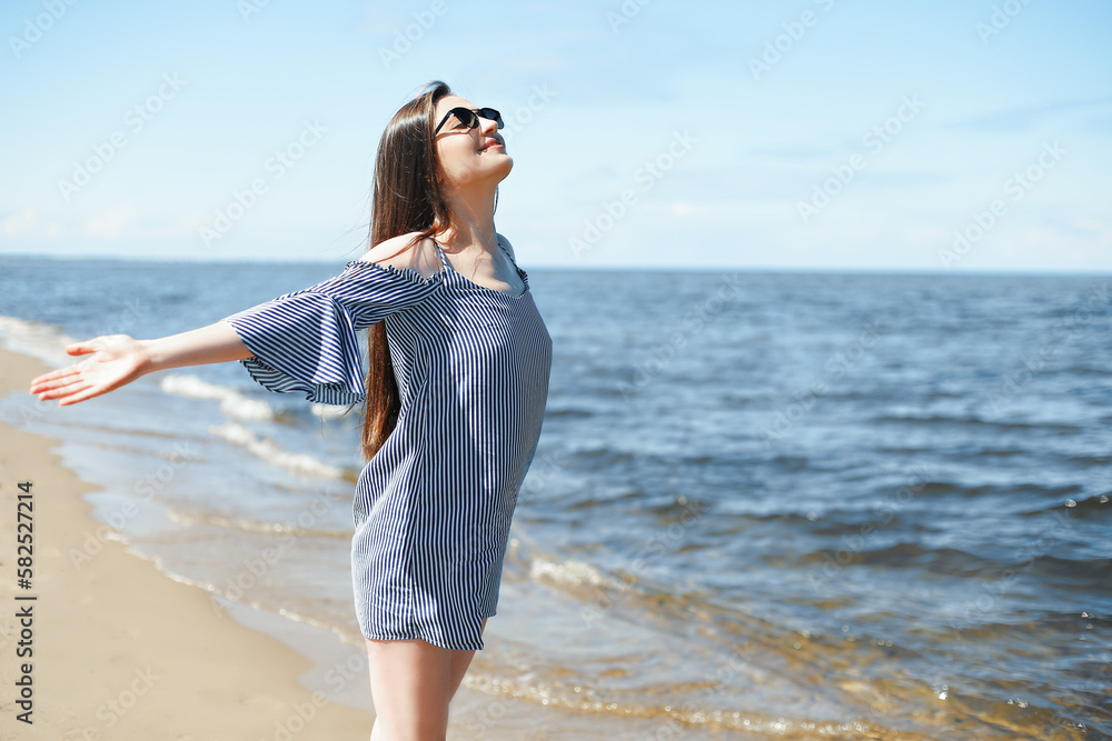 Happy smiling woman in free bliss on ocean beach standing with open hands. Portrait of a brunette female model in summer dress enjoying nature during travel holidays vacation outdoors
