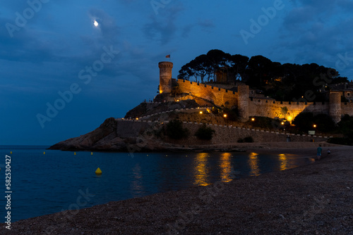 The medieval castle in Tossa de Mar, Spain, offers a breathtaking view of the beach and sea at night
