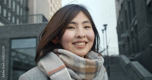 Close-up of an Asian girl smiling happily against the backdrop of city buildings. A young girl with black hair, looking directly at the camera. Natural beauty.