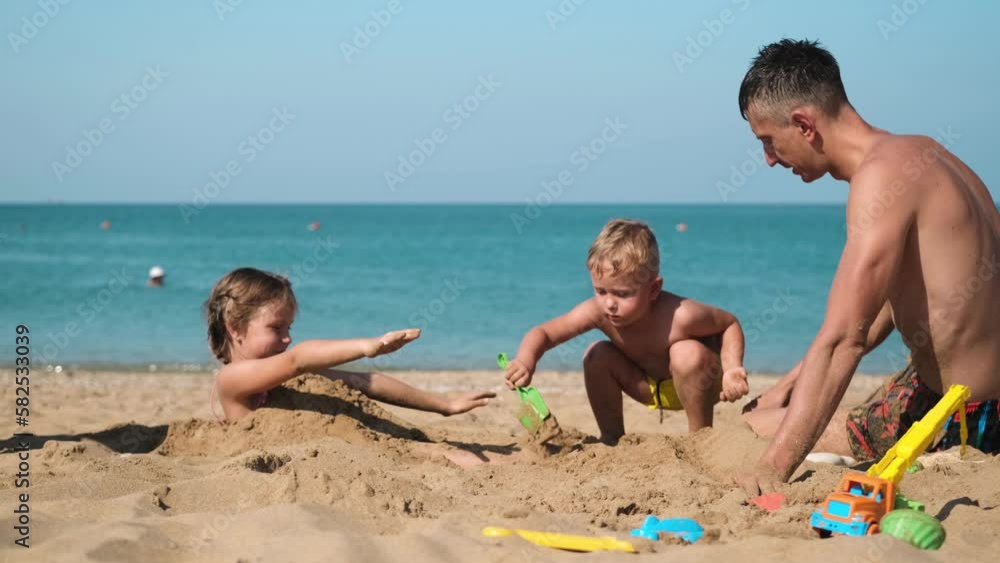 Children play with their father on the beach with sand. The family had fun at the seaside. Children play with their father on the beach with sand. The family had fun at the seaside.