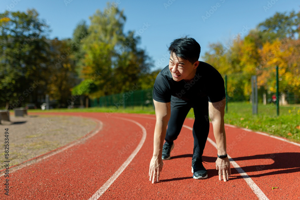 A young Asian man is an athlete, a runner. He is preparing for the start of the marathon, a race on the stadium's running track.