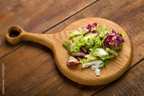 Leaves of green salad mix on a wooden board.