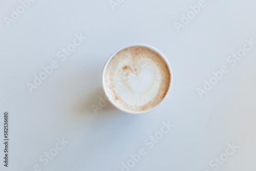 Delicious cappuccino in a paper cup on a white background view from above.