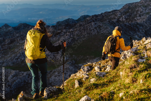 group of two mountaineers with backpack and trekking poles hiking up a mountain peak. sport, adventure and outdoor activity. weekend activities.