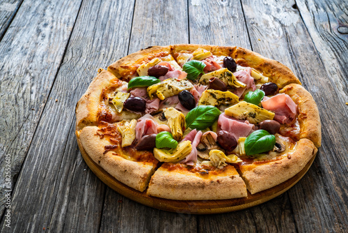 Pizza capricciosa with cooked ham, mozzarella, artichoke   and vegetables on wooden table
