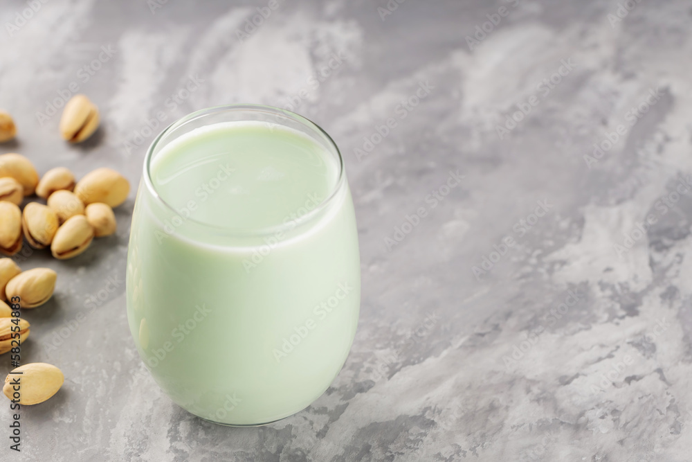 Organic non dairy pistachio milk in glass with pistachionuts on gray background. Vegan plant based milk. Copy space Organic non dairy pistachio milk in glass with pistachionuts on gray background. Vegan plant based milk. Copy space