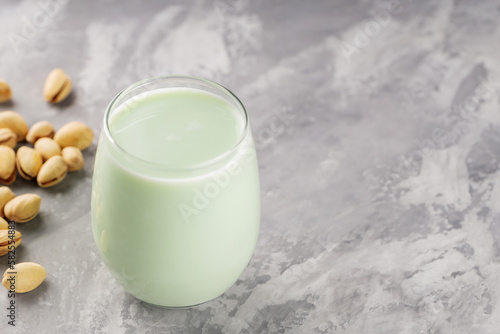 Organic non dairy pistachio milk in glass with pistachionuts on gray background. Vegan plant based milk. Copy space photo
