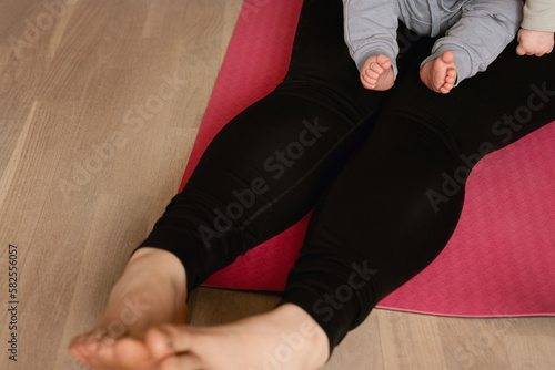 Baby and woman sitting on yoga mat. Concept of postpartum exercise, workout with baby or toddler. Active lifestyle with training after giving birth.