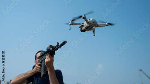 Fototapeta Naklejka Na Ścianę i Meble -  A man aims to shoot a rifle at a flying drone against a blue sky. 