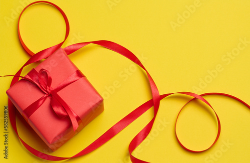 Square box tied with a red bow on a yellow background, top view