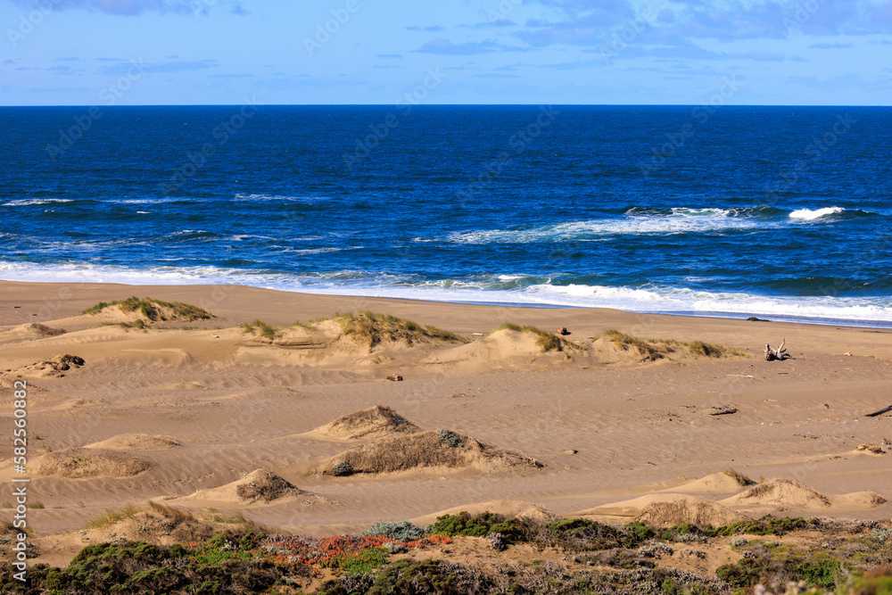 Small waves break on deserted sandy beach with blue water to the horizon