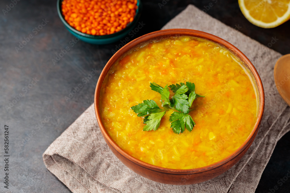 Red lentil Indian soup on a dark background. Bowl of lentil soup, ingredients and wooden spoon. Close up Red lentil Indian soup on a dark background. Bowl of lentil soup, ingredients and wooden spoon. Close up