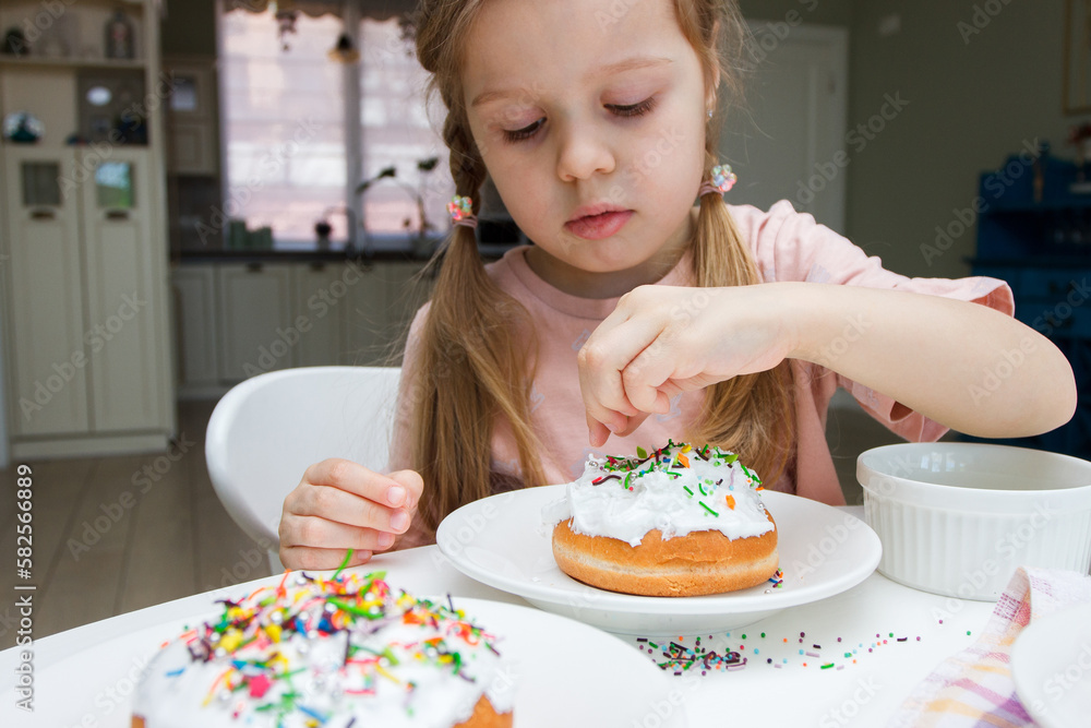 Little cute girl decorate a cake with sweet colored decorations, concept of cooking Little cute girl decorate a cake with sweet colored decorations, concept of cooking