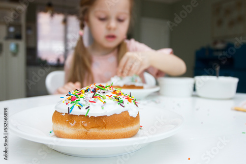 Little cute girl decorate a cake with sweet colored decorations, concept of cooking