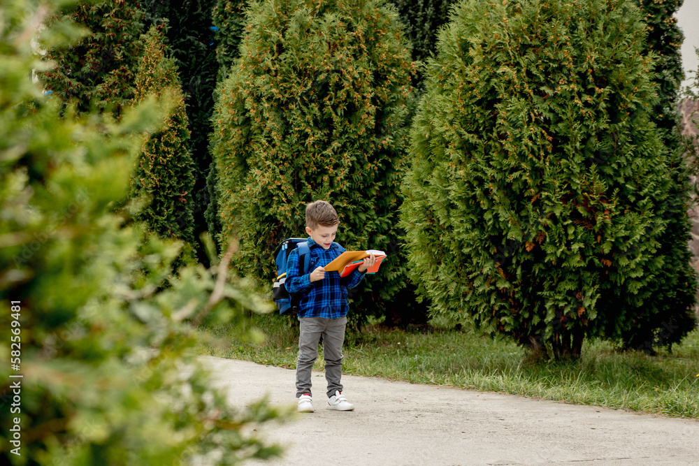 Little first grader with backpack looking the copybook, going home from school Little first grader with backpack looking the copybook, going home from school