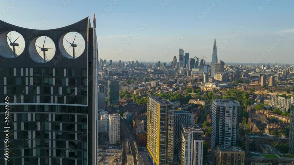 Top of famous high rise Strata building with wind turbines. Sliding reveal of cityscape at golden hour. Aerial hyper lapse shot. London, UK